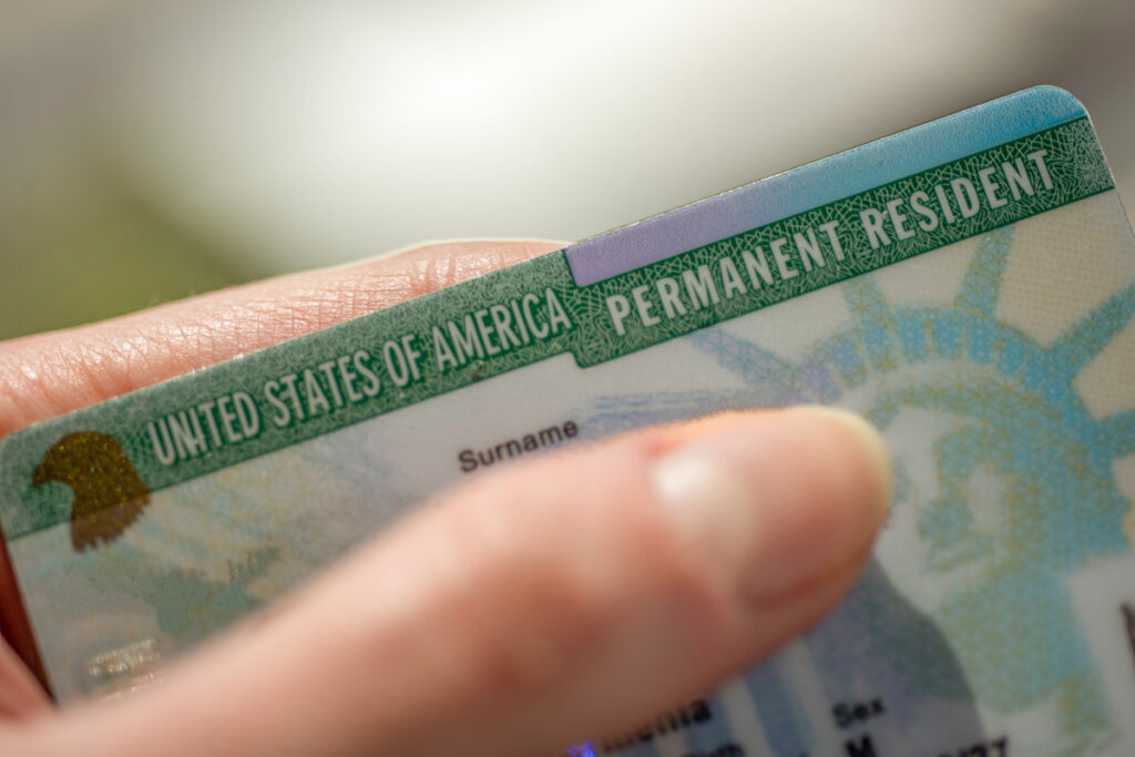 A United States Permanent Resident card being held between a person's thumb and forefinger